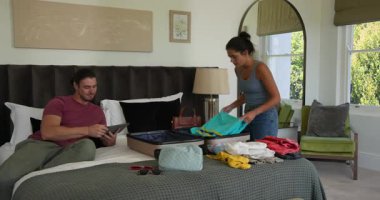 Tabletleri değiş tokuş eden bir çift, sonra kalkışa hazırlanırken giysilerini açık bavula koyuyor. Yaşam tarzı, seyahat, organizasyon, koordinasyon, daire, modern, gündelik