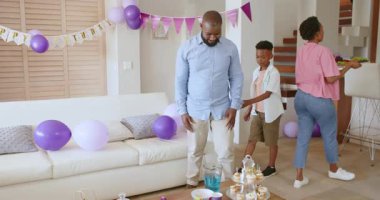 Oğlu evde doğum günü partisi için oturma odasını dekore ederken babam kek hazırlıyor. Kutlama, aile, pişirme, şenlik, neşe, hazırlık