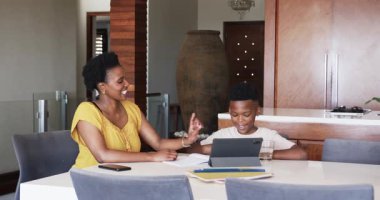 Anne oğluna ödevlerinde yardım ediyor, tablet ve not defteri kullanıyor. Ebeveynlik, eğitim, teknoloji, aile, öğrenme, bağlanma