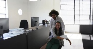 Mutlu meslektaşlar ofiste eğleniyor, erkekler modern ofiste kadınları ofis sandalyesine oturtuyor. İş, iletişim, iş, ofis çalışma ortamı kavramı.