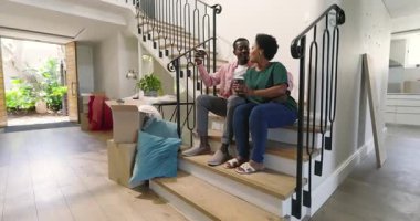 Birlikte kutuları açmak, merdivenlerde oturan farklı çiftler, evde kahve içmek. Yer değiştirme, ev, taşınma, yaşam tarzı, takım çalışması