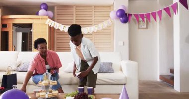 Evde doğum günü kutlaması, annesi gülümserken oğlu kornaya basıyor. Aile, kutlama, eğlence, neşe, bağ, mutluluk