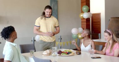 Partide, arkadaşlar yemek masasında içki içerler, yemekle ve kahkahalarla kutlamanın tadını çıkarırlar. toplanma, arkadaşlık, mutluluk, parti