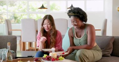 Afro-Amerikalı ve Asyalı arkadaşlar yemek odasında 30. doğum gününü pasta ve meyvelerle kutluyorlar. Kutlama, dostluk, doğum günleri, meyveler, pasta, modern, neşeli