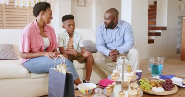 Evde doğum gününü kutlayan Afro-Amerikan ailesi hediyeler ve pastalarla oturuyor. Kutlama, parti, mutluluk, birliktelik, neşe