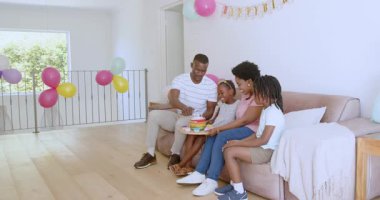 Parlak evde doğum gününü kutlayan, renkli pastalar tutan ve gülümseyen bir aile. Kutlama, balonlar, şenlik, coşku, birliktelik, neşe, ev, parti