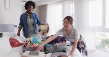 Çeşitli arkadaşlar modern otel odasında bavul hazırlıyor, giysileri düzenliyor ve akıllı telefonları kontrol ediyorlar. Seyahat, macera, paketleme, arkadaşlık, minimalist, otel, hazırlık, işbirliği