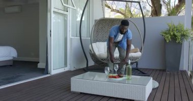 Çağdaş evin dışındaki ahşap güvertede sallanan sallanan sandalyede şarap ve çilek var. Rahatlama, açık hava, davet, minimalizm, yaşam tarzı, sükunet, doğa, konfor