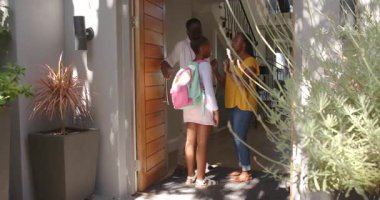 Afro-Amerikan ailesi yeni çocuğu pembe sırt çantası ve saksı bitkisiyle karşılıyor. Evlat edinme, vesayet, aile, destek, ev, mutluluk, birliktelik, etkileşim