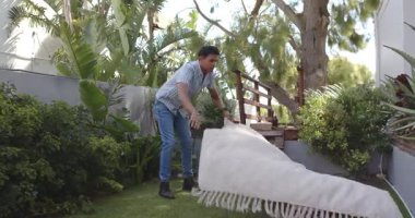 Genç erkek, arka bahçedeki ahşap merdivenlerin yanında hafif kumaşla ahşap yapı kaldırıyor. Açık hava, tropikal, yeşillik, işçilik, verimlilik, uyum, rahatlama, güneş ışığı, bahçıvanlık.