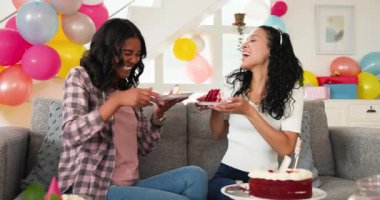 Farklı bayan arkadaşlar oturma odasındaki gri kanepede balonlarla pasta ve patlamış mısır yiyorlar. Doğum günü, kutlama, parti, şenlik, konfor, iç mekan, atıştırma