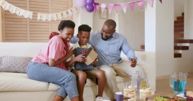 Evde doğum günü kutlaması, Afro-Amerikan ailesinin açılış hediyesi neşeli ifadelerle. Kutlama, mutluluk, hediye, parti, oturma odası, sürpriz