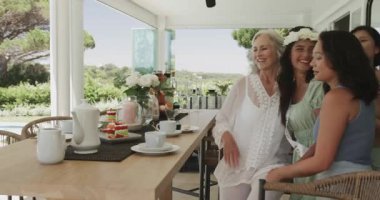 Çeşitli bayan arkadaşlar ahşap masa kenarından akıllı telefon alıp verandada selfie çekiyorlar. Arkadaşlık, kutlama, eğlence, açık hava, yaşam tarzı, dostluk, coşku.