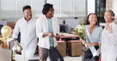 Afrika kökenli Amerikalı meslektaşlar ofiste kuşak takan kadını buket ve kartla kutluyorlar. Başarı, tanınma, çalışma alanı, takım çalışması, alkış, hediye, dizüstü bilgisayarlar