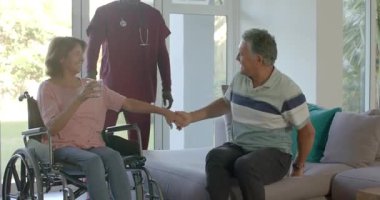 Erkek hemşire yaşlı kadını evde iterken partnerler su ve hemşire de tekerlekli sandalyeyi ayarlıyor. Bakıcı, yaşlı, yoldaş, ev, sağlık, destek, sıcak