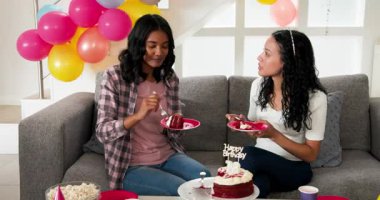 Çeşitli bayan arkadaşlar oturma odasında renkli balonlarla kırmızı kadife kekin üstüne pasta koyuyorlar. Doğum günü, kutlama, kilometre taşı, parti, gençlik, yaşam tarzı, modern