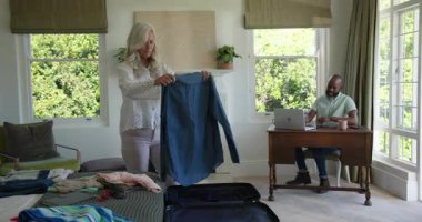 Yaşlı çift tableti incelerken yatak odasında bavul bavul hazırlıyor. Seyahat, paketleme, organizasyon, işbirliği, yaşam tarzı, ev ofisi, boş zaman