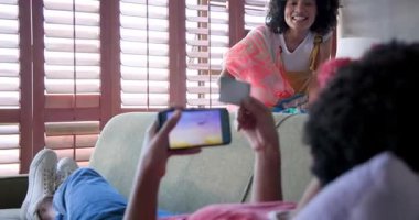 Evde dinlenen, arka planda çamaşırları katlarken akıllı telefon kullanan bir kadın. ev hayatı, çoklu görev, teknoloji, iletişim, boş zaman, ilişki