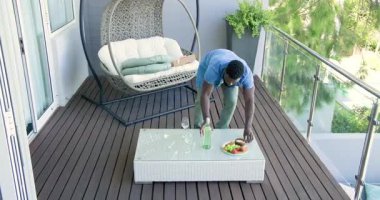 Kırık parçaları fark ettim, Afro-Amerikalı adam kırıkları kaldırıyor, minderleri hareket ettiriyor ve balkondan meyve topluyor. Rahatlama, açık havada yaşam, çağdaş, boş zaman, yaşam tarzı, refah, sükunet