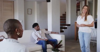 Arkadaşlar modern oturma odasında sohbetin tadını çıkarıyorlar, gülümsüyorlar ve rahatlıyorlar. Arkadaşlık, birliktelik, rahatlama, toplanma, ev, rahat