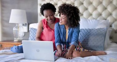 Anne ve kızı evde dizüstü bilgisayar kullanırken birlikte gülüyorlar. Aile, bağ, teknoloji, rahatlama, mutluluk, rahatlık.