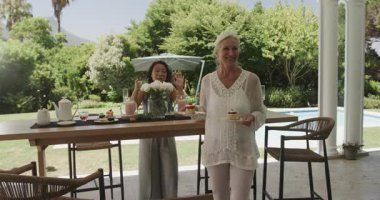 Çeşitli bayan arkadaşlar brunch 'ı hazırlamak için hamur işleri ve teras masasına kahve koyuyorlar. Arkadaş canlısı, kutlama, açık hava, zarafet, konukseverlik, boş zaman, sosyalleşme.