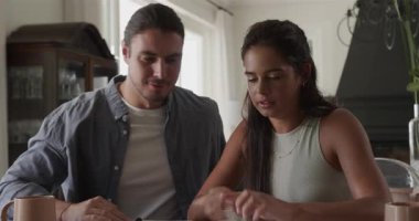 Yemek masasına gelen çift, bütçe planlaması, zarf düzenleme ve çizelgeleri gözden geçirme gibi işler yapıyor. İşbirliği, takım çalışması, planlama, organizasyon, ev ofisi, modern, samimi