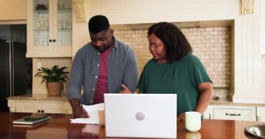 Afro-Amerikalı çift mutfak tezgahında dizüstü bilgisayarlarıyla belgeleri inceliyor. Finans, bütçe, teknoloji, takım çalışması, ev ofisi, yaşam tarzı