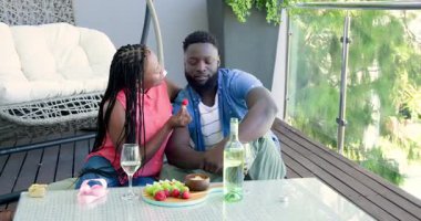 Balkona gelip çilek besleyen, romantizmi kutlayan şarap içen Afro-Amerikan çifti. Romantizm, samimiyet, rahatlık, yaşam tarzı, zarafet, rahatlama, kutlama