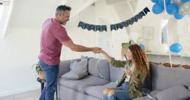 Tavan penceresinin altında balonlarla dans etmeden önce koltukta kadeh tokuşturup doğum gününü kutlayan bir çift. Romantik, kutlama, dans, şenlik, çatı katı, neşe, yakınlık