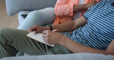 Afro-Amerikalı çift kanepede dinleniyor, evde tabletin tadını çıkarıyorlar. Teknoloji, eğlence, bağlanma, ilişki, mutluluk, yaşam tarzı