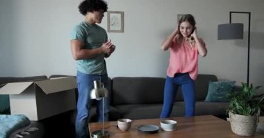 Genç çift yeni evlerinde kutuları açıyor ve oturma odasını düzenliyor, mutlu bir şekilde gülümsüyorlar. Taşınma, yeni başlangıçlar, dekorasyon, taşınma, aile, ev hayatı