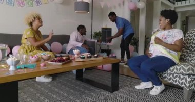 Çeşitli arkadaşlar evde bebek partisini kutluyor, alkışlıyor ve hediyeleri neşeyle açıyor. Kutlama, parti, mutluluk, heyecan, aile, toplanma