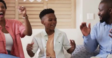 Aile evde birlikte güzel vakit geçirir, kanepede alkışlar ve gülümserler. Mutluluk, oturma odası, birliktelik, ebeveynlik, kaynaşma, rahatlık