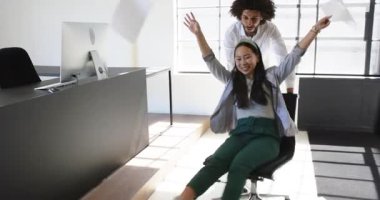 Mutlu meslektaşlar ofiste eğleniyor, erkekler modern ofiste kadınları ofis sandalyesine oturtuyor. İş, iletişim, iş, ofis çalışma ortamı kavramı.