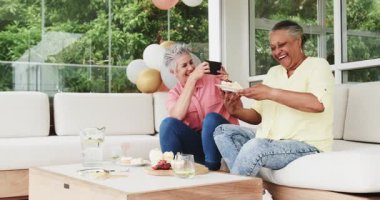 Son sınıf arkadaşları evde rahat bir terasta taç ve balon tutarak sohbet edip kutluyorlar. Kutlama, dostluk, konfor, coşku, neşe, toplanma, nostalji, birliktelik.