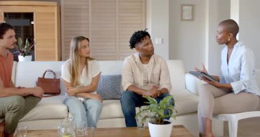 Çeşitli arkadaşlar sıcak oturma odasında tabletle düşünceli bir şekilde tartışıyorlar. Çeşitlilik, arkadaşlık, sohbet, teknoloji, yaşam tarzı, daire