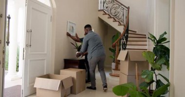 Mutlu siyah kadın ve erkek karton kutuları açıyor, duvara resim asıyor, güneşli bir günde yeni bir eve taşınıyor. Yeni ev, mülk, mutluluk, yaşam tarzı ve ilişki kavramı.