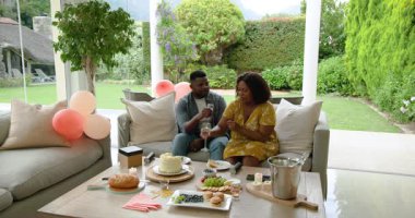 Şampanya ve pastayla kutlayan Afro-Amerikan çift birlikte terasta. Kutlama, mutluluk, açık hava, neşe, şenlik, romantizm