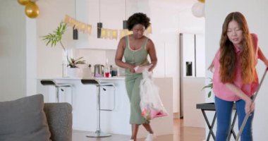 Afro-Amerikalı ve Asyalı arkadaşlar oturma odasını temizliyor, üzüm ve şarapla masayı düzenliyorlar. Kutlama, dostluk, düzenlilik, rahat, şenlikli, toplanma, takım çalışması, dekor