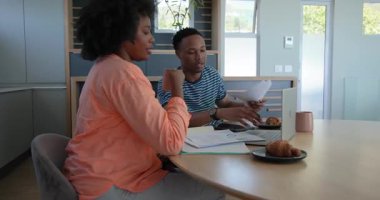 Afro-Amerikalı çift evde laptopları ve kahve fincanlarıyla iş konuşuyorlar. Evden çalışma, işbirliği, ortaklık, teknoloji, tartışma, takım çalışması