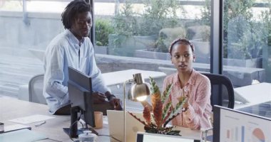 Afro-Amerikalı iş arkadaşları bilgisayarları tıklatan, çizelgeleri gözden geçiren kadınlardan sonra masadaki başarıyı kutluyorlar. İşbirliği, takım çalışması, yenilik, çeşitlilik, üretkenlik, iletişim, modern