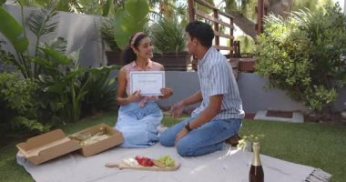 Çeşitli çiftler iyi korunmuş bahçede tebrik kartı ve meyve tabağıyla yıldönümlerini kutluyorlar. Kutlama, romantizm, mutluluk, bahçe, birliktelik, piknik, aşk, neşe