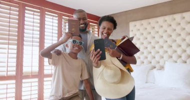 Aile tatilden zevk alıyor, pasaportları tutuyor ve otel odasında birlikte gülümsüyor. Seyahat, turizm, tatil, konukseverlik, valiz, macera