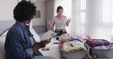 Afro-Amerikalı ve Asyalı arkadaşlar otel odasında bavul, kitap ve gözlüklerle toplanıyorlar. Paketleme, arkadaşlar, seyahat, otel, eğlence, hazırlık, yaşam tarzı, macera