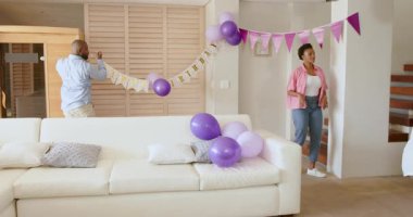 Evinde kutlama için mor balonlar ve afişlerle oturma odasını dekore eden bir adam. Dekorasyon, parti, festival, ev, etkinlik, hazırlık