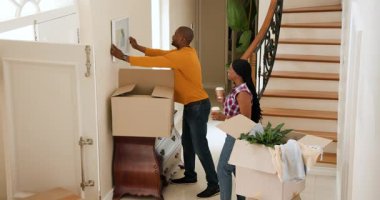 Koridordaki karton kutulardan duvara resim asan mutlu siyah kadın ve adam güneşli bir günde yeni bir eve taşınıyor. Yeni ev, mülk, mutluluk, yaşam tarzı ve ilişki kavramı.
