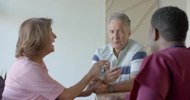 Önlüklü hemşirenin hidrasyon için getirdiği suyu yudumlayan çeşitli yaşlı çiftler. Nesiller arası, arkadaşlık, bakım, sağlık, sağlık, iletişim, duygusal