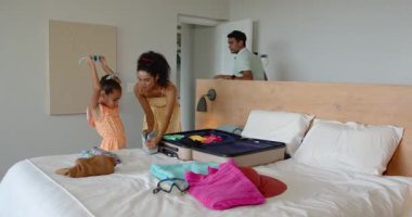 Çeşitli aileler açık bavullarını parlak, havadar evlerinde topluyor seyahat planlarını ve aksesuarlarını kontrol ediyorlar. Tatil, planlama, seyahat, aile, aksesuarlar, parlak, neşeli, ev, toplanma