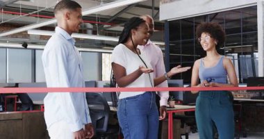 Modern ofis içinde çeşitli meslektaşlar dizüstü bilgisayarlar kullanarak ve gülümseyerek kurdele kesiyor. Takım çalışması, kutlama, işbirliği, girişimcilik, çalışma alanı, modern, başarı